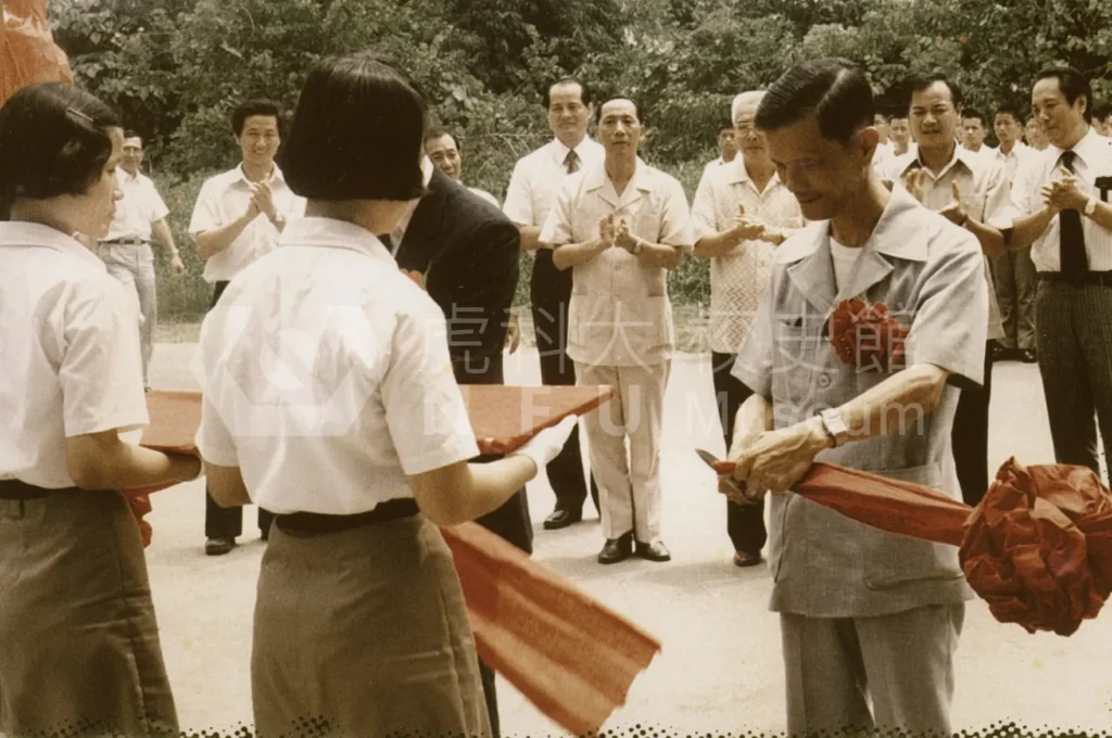 One person is cutting the ribbon，with a group of people applauding behind。